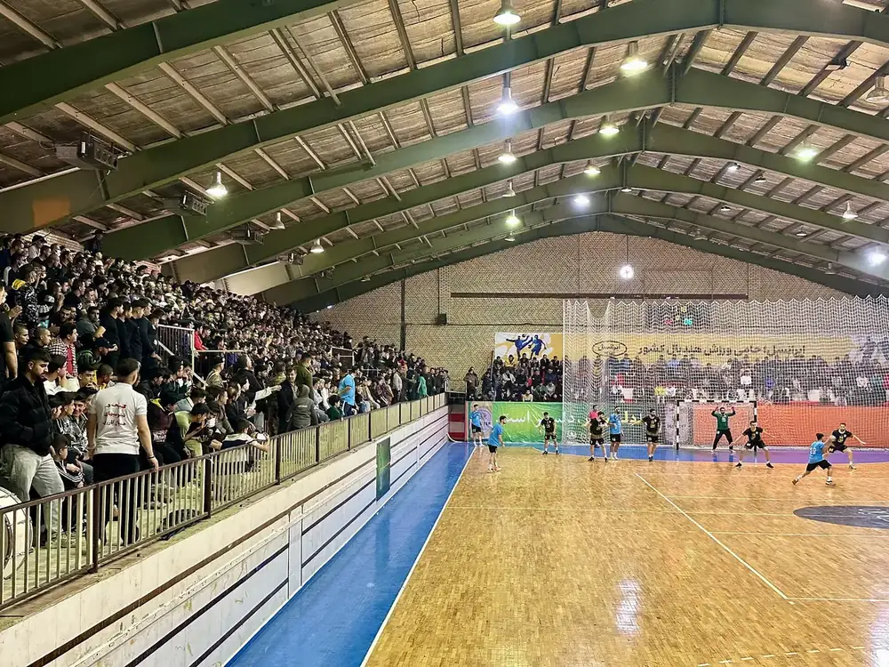 Blick über eine Sporthalle mit Parkettboden, farbiger Markierung und besetzten Rängen